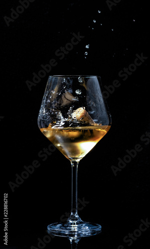 dry white grape wine poured into a glass with a crust poured with splashes on a black background