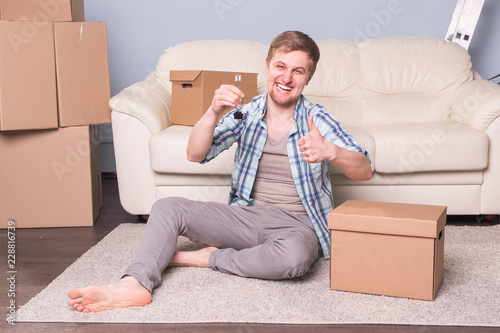 New home, real estate owner and moving concept - Young man holding keys of new home and showing thumb up