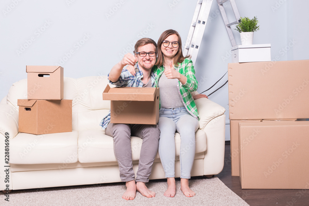 Moving, relocation and new home concept - young couple having fun on the couch surrounded with boxes Moving, relocation and new home concept - young couple having fun on the couch surrounded with boxes