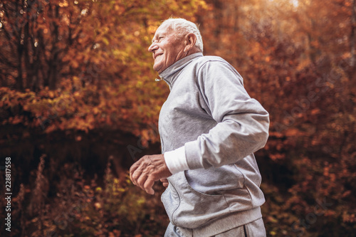 Senior runner in nature. Elderly sporty man running in forest during morning workout. Healthy and active lifestyle at any age concept