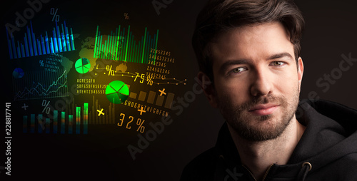 Portrait of a young businessman with colorful charts and graphs next to him on a dark background