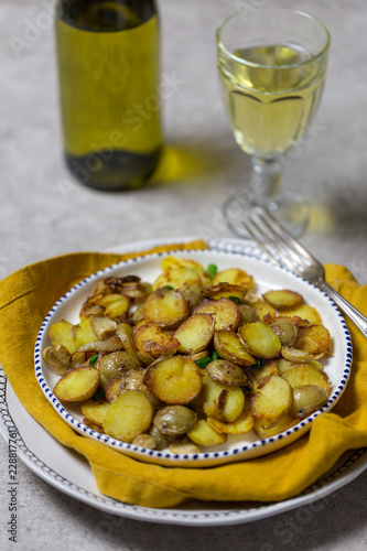 Fried potatoes with mushrooms and onion in white plate with vine at gray background for holiday dinner