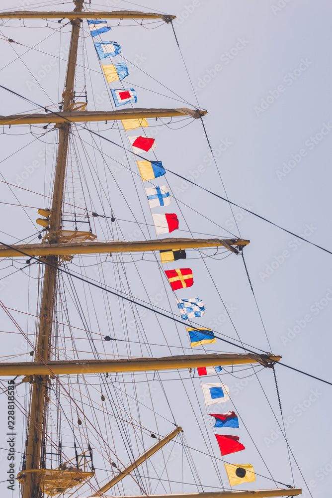 Fototapeta premium Colorful nautical sailing flags flying in the wind from the lines of a sailboat mast backlit in bright blue sky by the cloudy stormy day. Retro toned.