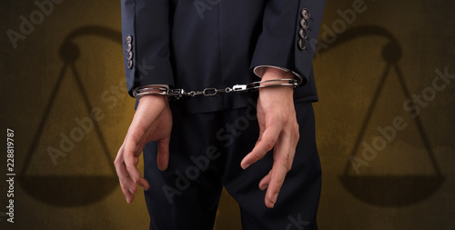 Arrested businessman in handcuffs with hands behind back and justice symbol wallpaper 