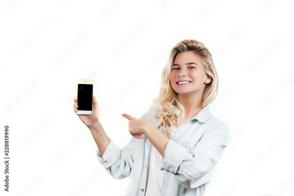 very beautiful young girl points to the smartphone, standing on a white isolated background. very beautiful young girl points to the smartphone, standing on a white isolated background.