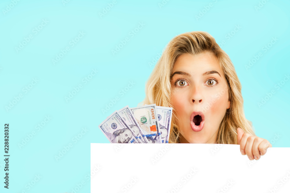 very beautiful bright girl in Christmas clothes peeking out of a white box with money in her hand on a blue isolated background very beautiful bright girl in Christmas clothes peeking out of a white box with money in her hand on a blue isolated background