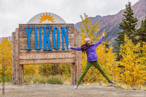 Yukon territory welcome sign - happy tourist woman jumping of fun in canadian territories. Alaska cruise travel autumn holiday. photo