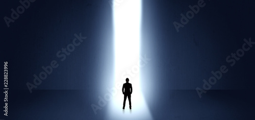 Businessman standing and seeing the light at the end of a big wall 