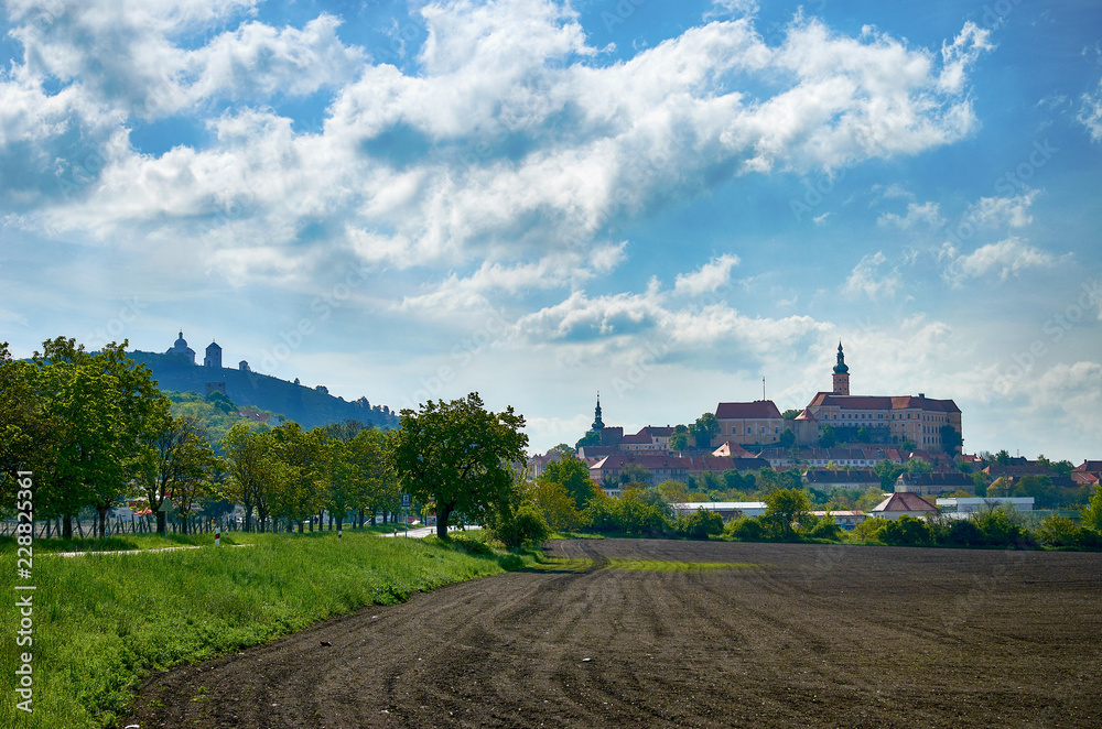 View of the town of Mikulov in South Moravia in the Czech Republic, with a monastery, church and chapel. With a field and a path in the foreground, under a blue sky with clouds