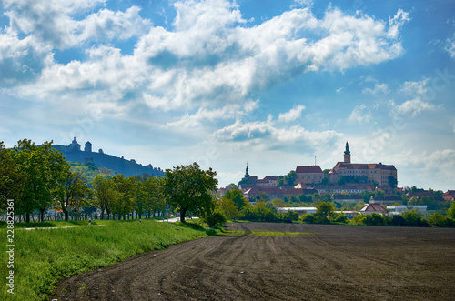 View of the town of Mikulov in South Moravia in the Czech Republic, with a monastery, church and chapel. With a field and a path in the foreground, under a blue sky with clouds