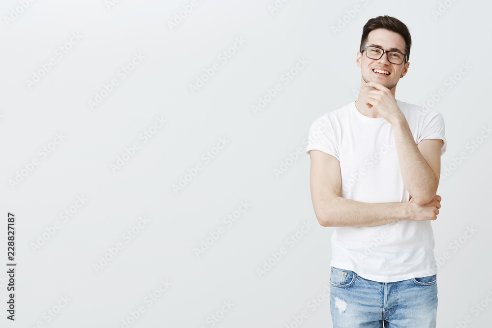 Portrait of guy pleased and delighted with great result of work rubbing chin smiling self-satisfied and joyful, having lots ambitious thoughts in mind, standing happy against gray background