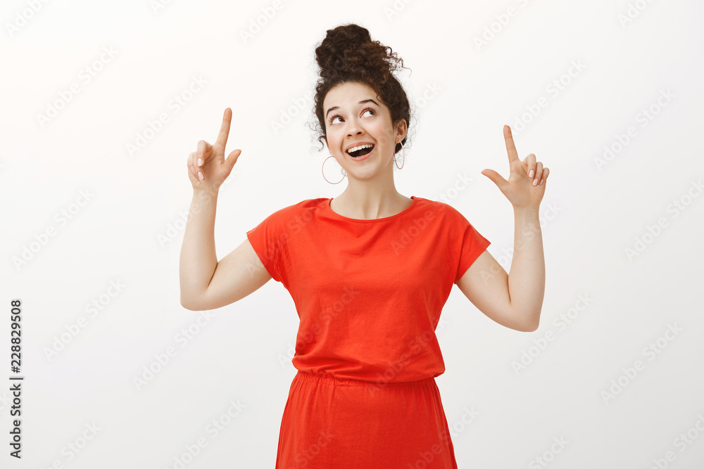 Studio shot of dreamy good-looking female with curly hair, looking and pointing up with happy joyful expression, feeling great and dreaming about future date with boyfriend over gray background Studio shot of dreamy good-looking female with curly hair, looking and pointing up with happy joyful expression, feeling great and dreaming about future date with boyfriend over gray background