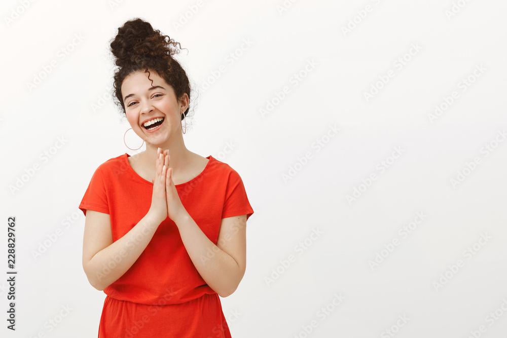 Carefree beautiful female sibling in trendy red dress, holding hands in pray or rubbing palms over chest while laughing out loud and feeling great, asking coworker help or favour over gray wall Carefree beautiful female sibling in trendy red dress, holding hands in pray or rubbing palms over chest while laughing out loud and feeling great, asking coworker help or favour over gray wall