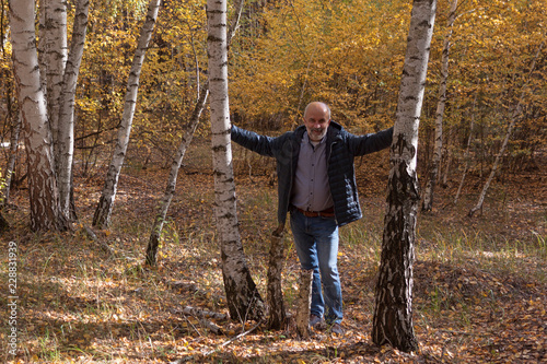 A man of mature age in a Birch grove next to two trees