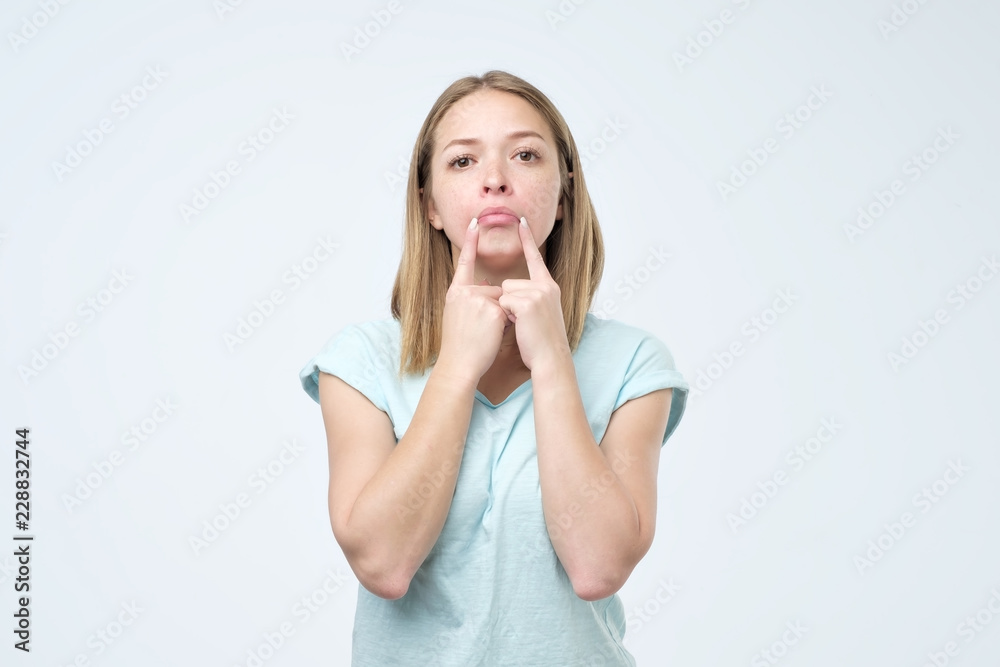 Caucasian woman trying to make fake smile with her fingers stretching the corners of her mouth. Caucasian woman trying to make fake smile with her fingers stretching the corners of her mouth.
