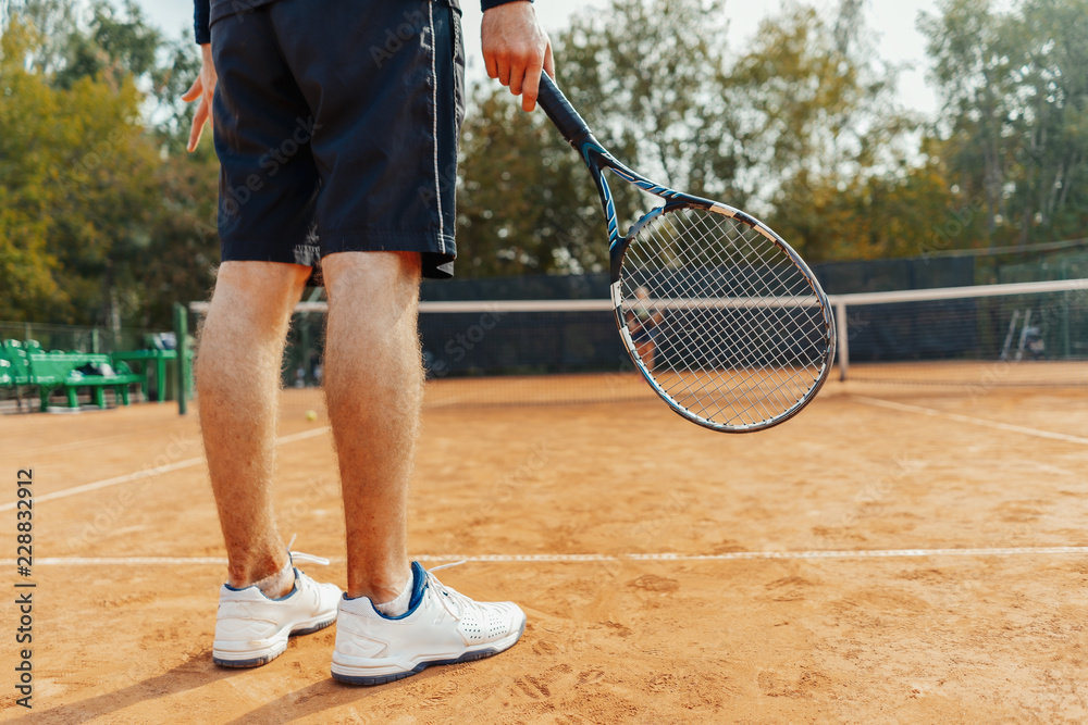 Close up of man holding racket while waiting for ball serving at tennis court.