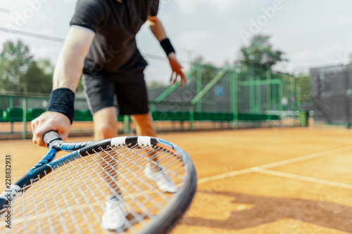 Close up of man holding racket at right hand and beating a tennis ball.