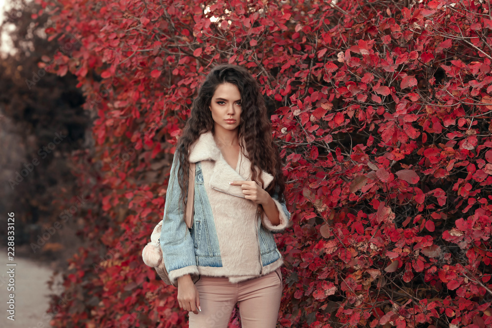 Fashionable Woman look autumn outdoor portrait. Young beautiful brunette in jeans jacket with fur collar posing in red leaves park. Attractive girl in trendy casual clothes posing at camera. Fashionable Woman look autumn outdoor portrait. Young beautiful brunette in jeans jacket with fur collar posing in red leaves park. Attractive girl in trendy casual clothes posing at camera.