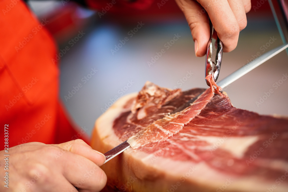 Obraz premium Professional cutter carving slices from a whole bone-in serrano ham