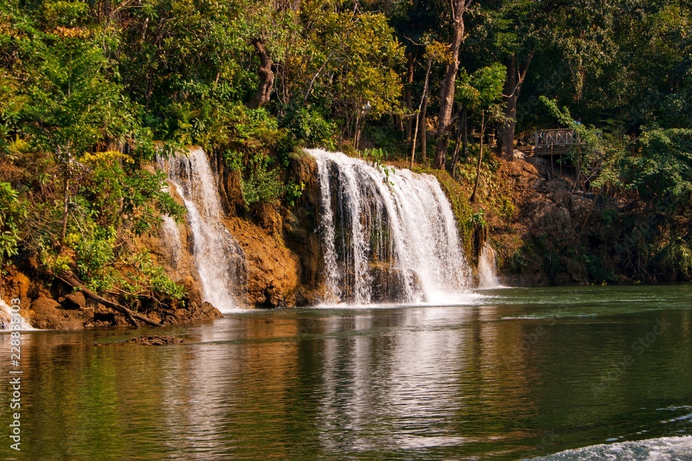 view of long-tail boat and raft house with many tourist playing in Kwai Noi River and Say Yok Yai Waterfall with green forest background, Kanchanaburi, west Thailand