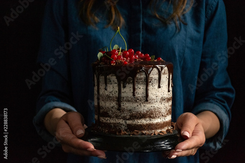 Chocolate puff cake with currants in the hands of a woman, dark background