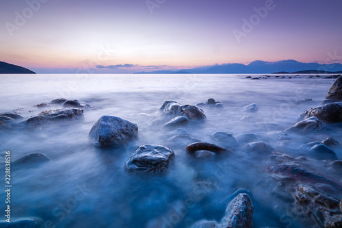 Long exposed photo of stones in the water of Mediterranean sea at sunrise. Crete, Greece