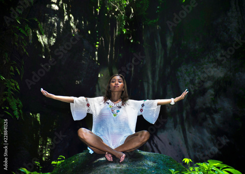 young beautiful and happy Asian practicing yoga outdoors at amazing peaceful and fresh tropical background sitting in rock doing relaxation and meditation exercise