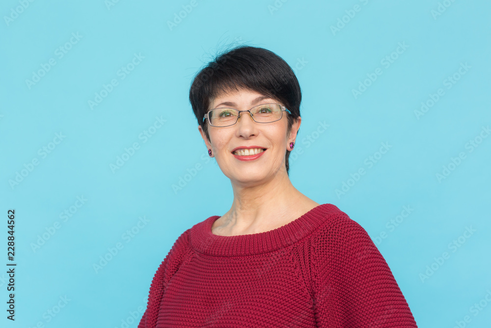 Middle-aged charming woman in red sweater posing on blue background Middle-aged charming woman in red sweater posing on blue background