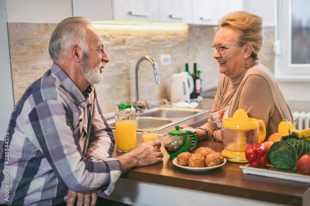 Elderly couple in the kitchen preparing breakfast. They drink coffee or tea and talk Elderly couple in the kitchen preparing breakfast. They drink coffee or tea and talk