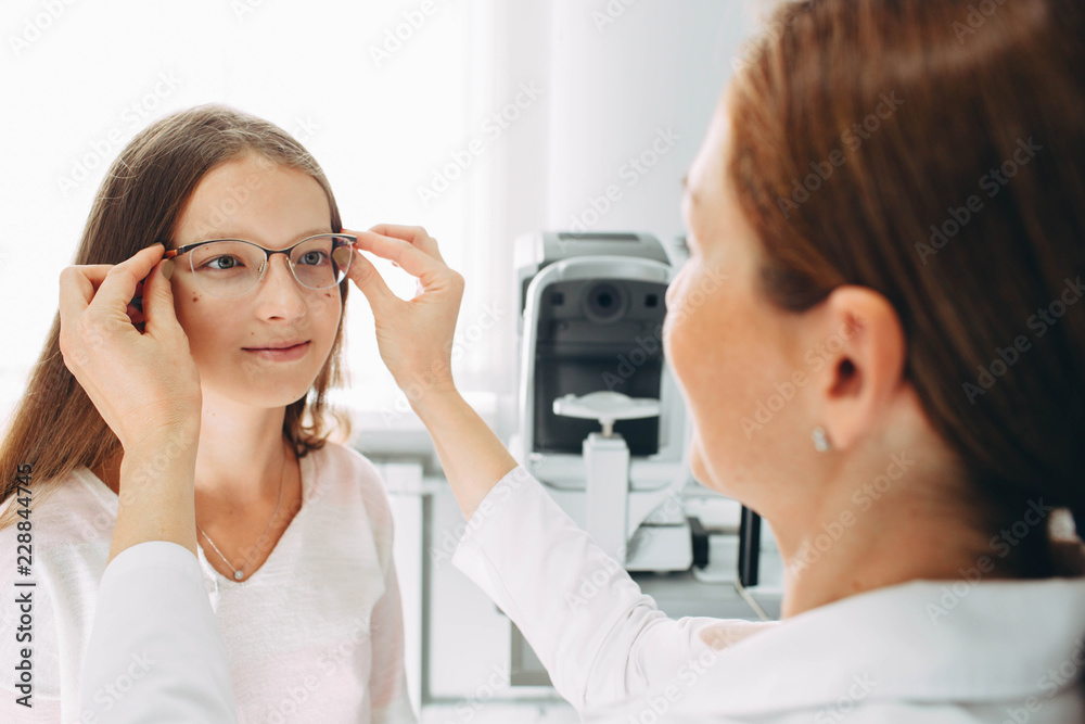 happy girl teenage having a new eyeglasses at doctor office. Optometrist ajusting eyeglases on girl's face. happy girl teenage having a new eyeglasses at doctor office. Optometrist ajusting eyeglases on girl's face.