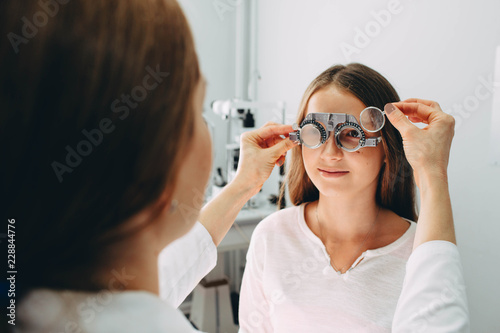 Optician doctor examining twelve age girls vision, using a trial frame