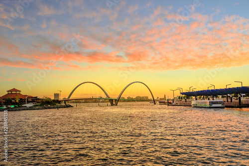 Fototapeta Naklejka Na Ścianę i Meble -  Scenic landscape of Elizabeth Quay Bridge on Swan River in Elizabeth Quay marina. The arched bridge is a new tourist attraction in Perth, Western Australia. Sky with red clouds of sunset.