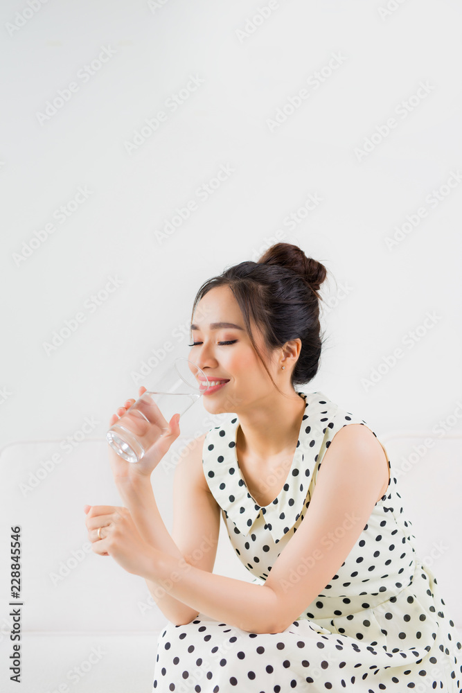 Young beautiful asian woman holding a glass of water while sitting at home Young beautiful asian woman holding a glass of water while sitting at home