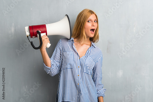Blonde girl holding a megaphone on textured grunge wall background