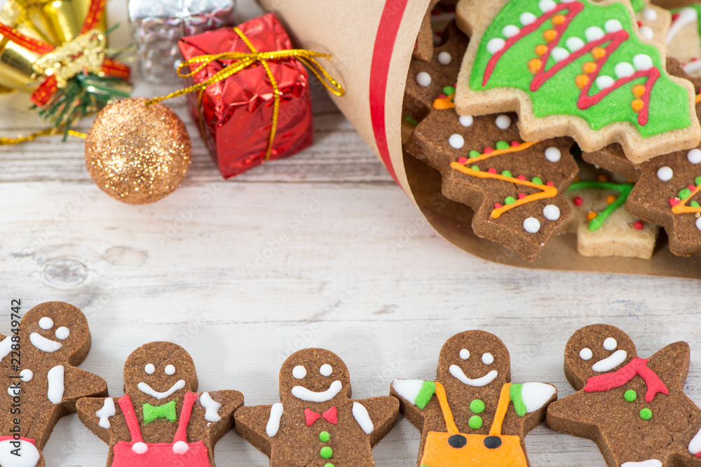 Tasty and cute baked Christmas cookies (gingerbread) with beautiful xmas decoration in paper bag on light wooden table background, close up, copy space (text space)