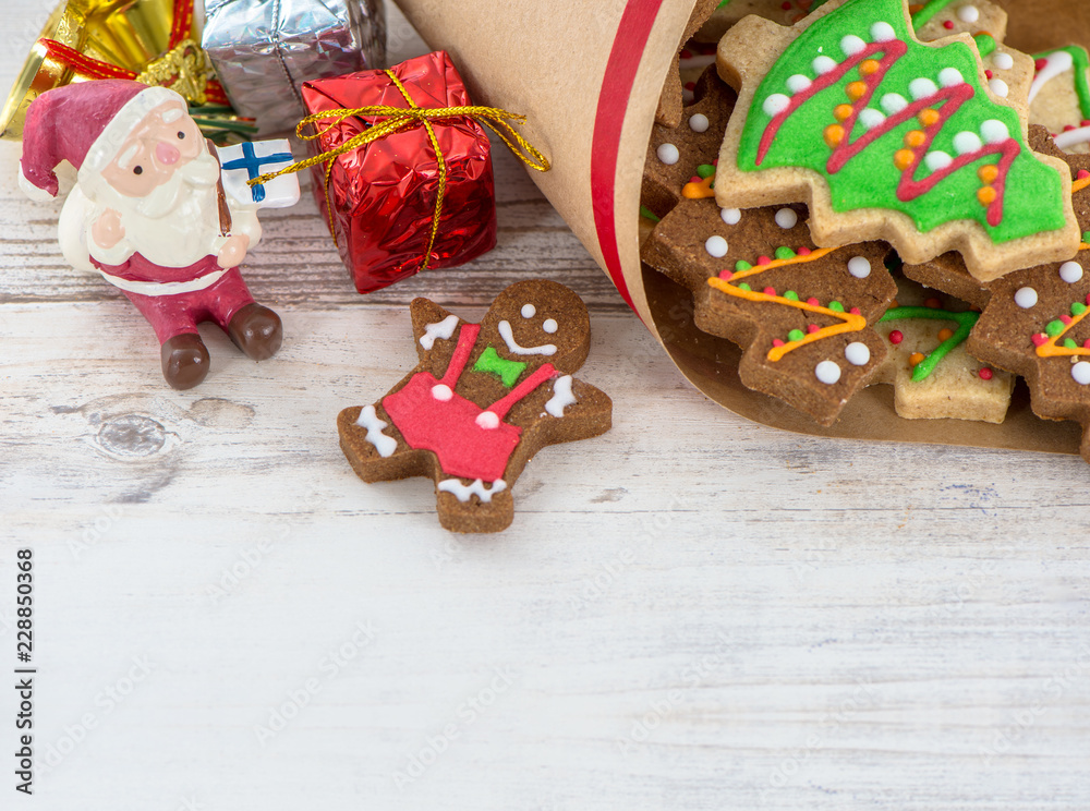 Tasty and cute baked Christmas cookies (gingerbread) with beautiful xmas decoration in paper bag on light wooden table background, close up, copy space (text space)