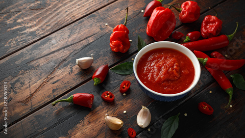 spicy hot sweet chili sauce with mix of chilli pepper, garlic and tomatoes on rustic wooden background photo