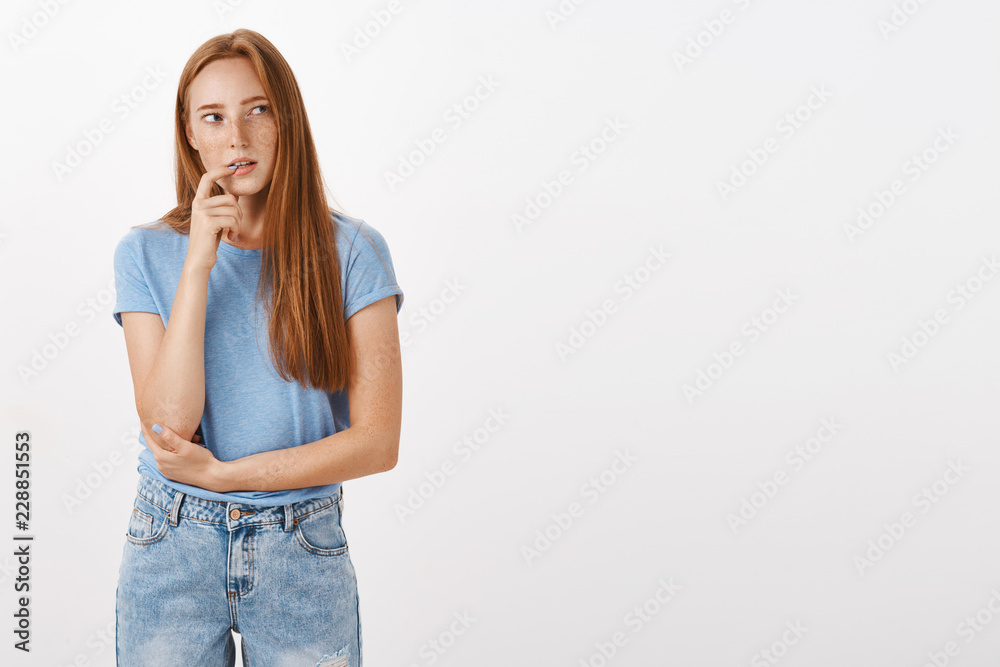 What if I order junk food. Thoughtful concentrated and curious redhead woman in blue t-shirt and jeans biting finger intrigued looking right while thinking having desire or interest in something What if I order junk food. Thoughtful concentrated and curious redhead woman in blue t-shirt and jeans biting finger intrigued looking right while thinking having desire or interest in something