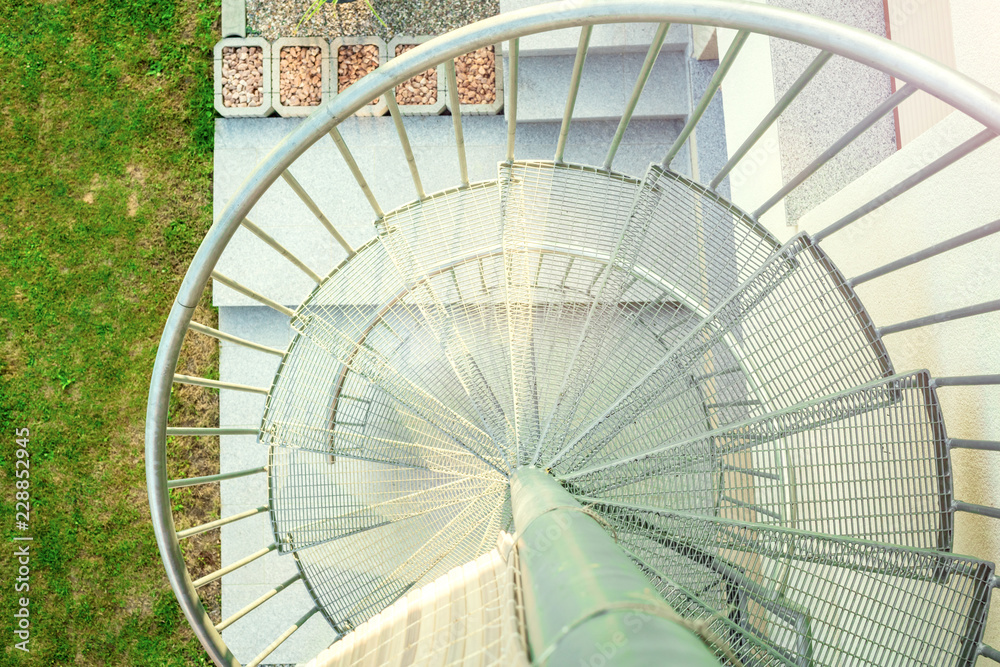 round staircase with steel steps and railings, top view, green grass in the yard background