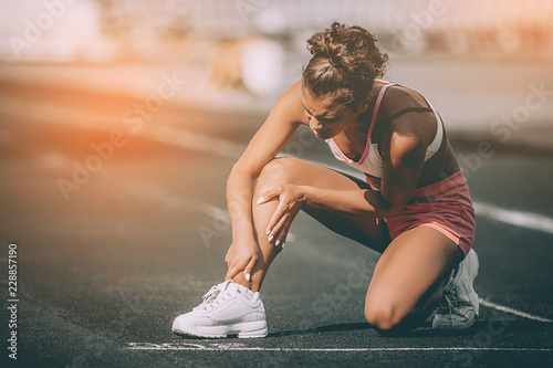 Close up portrait of sporty woman having knee injury in running track., Healthcare and sport concept. Sunshine background