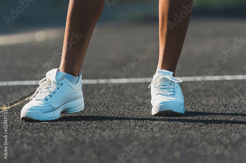 Woman's legs in white running shoes standing on asphalt