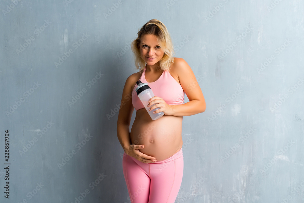Obraz premium Blonde pregnant woman doing sport with a bottle of water
