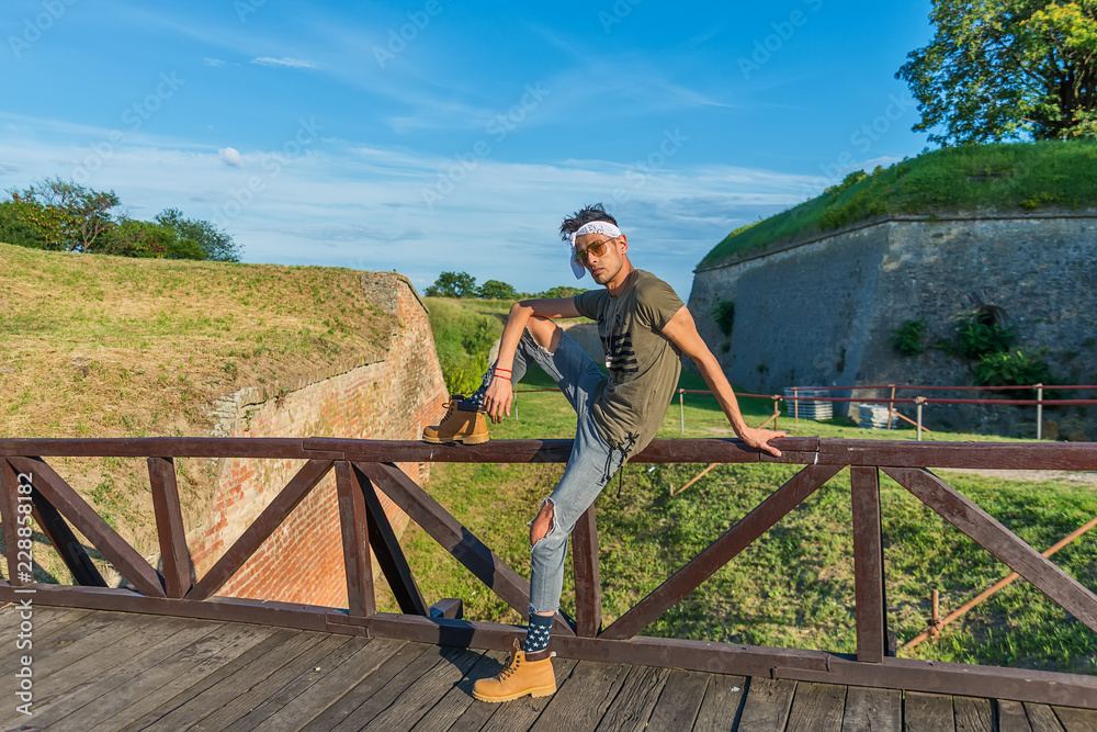 Extravagant (hipster) male model with sunglasses and a white scarf on a wooden bridge.