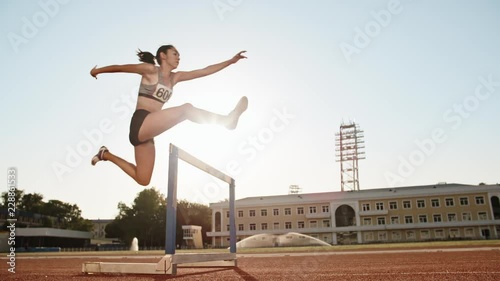 Female athlete on track. Young asian runner running on track of stadium, jumping over barriers, preparing for competition photo