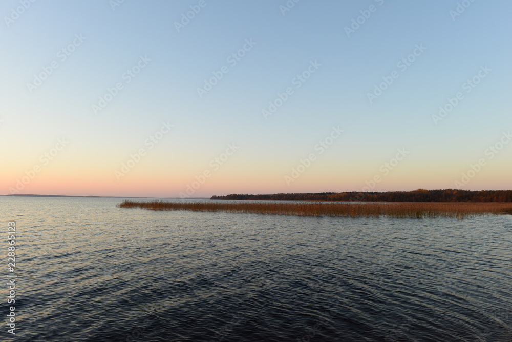 Blue sky with bright colors of sunset afterglow on a forest lake on an autumn evening