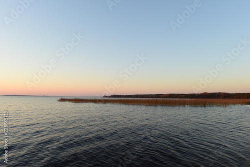 Blue sky with bright colors of sunset afterglow on a forest lake on an autumn evening