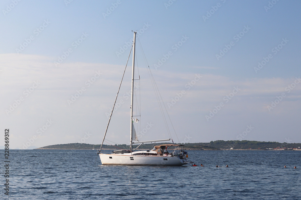 A modern sailing yacht is anchored in a bay. People bathe in the sea. Active rest on the Adriatic Sea of the Mediterranean region. Dalmatian riviera of Croatia. Prestigious and rich lifestyle A modern sailing yacht is anchored in a bay. People bathe in the sea. Active rest on the Adriatic Sea of the Mediterranean region. Dalmatian riviera of Croatia. Prestigious and rich lifestyle