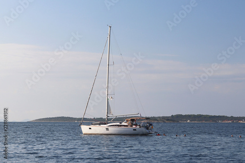 A modern sailing yacht is anchored in a bay. People bathe in the sea. Active rest on the Adriatic Sea of the Mediterranean region. Dalmatian riviera of Croatia. Prestigious and rich lifestyle