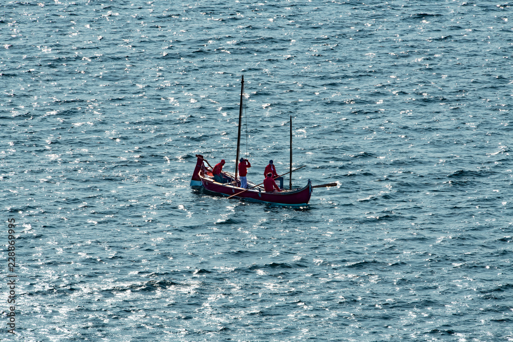 Obraz premium Barca a remi rossa, con persone che osservano in lontananza, in mezzo al mare