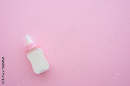 Top view of baby toddler feeding plastic bottle and soft teat with milk on pink background with copy space. Newborn accessories prepare for baby girl or toddler from day one, breastfeeding concept.